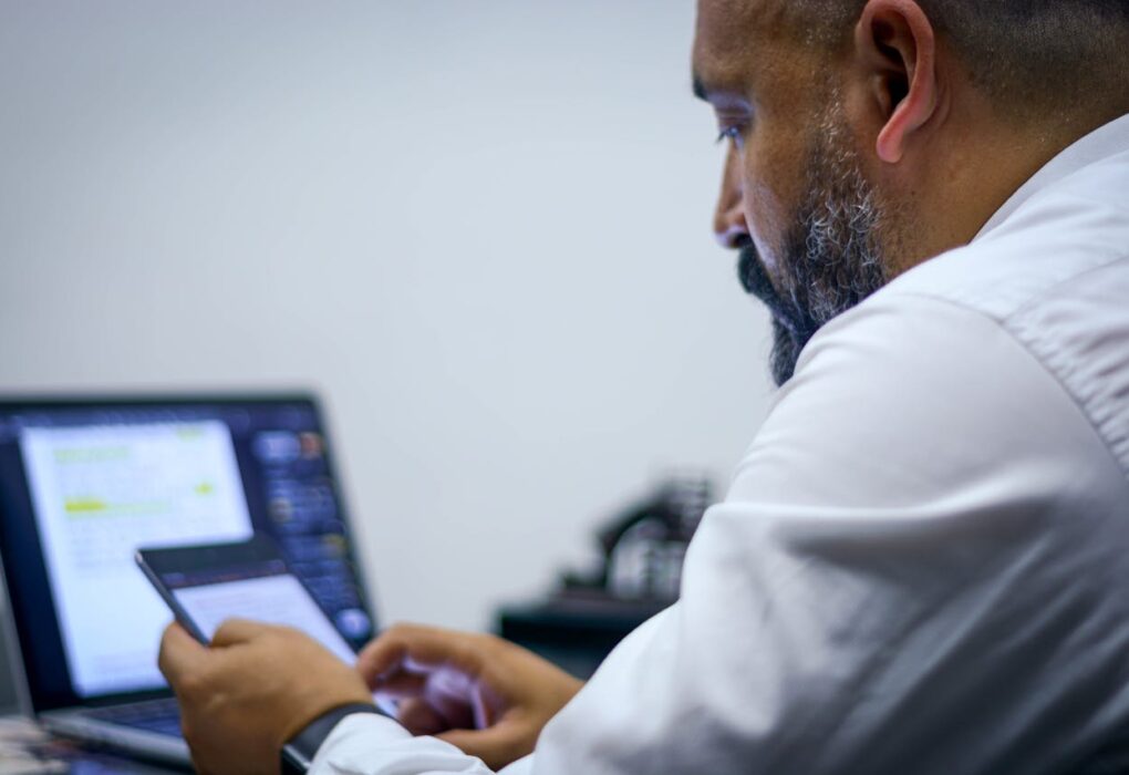 Un hombre de negocios sentado en su escritorio, mirando una tableta con una computadora portátil frente a él para representar las tendencias digitales en Ecuador.